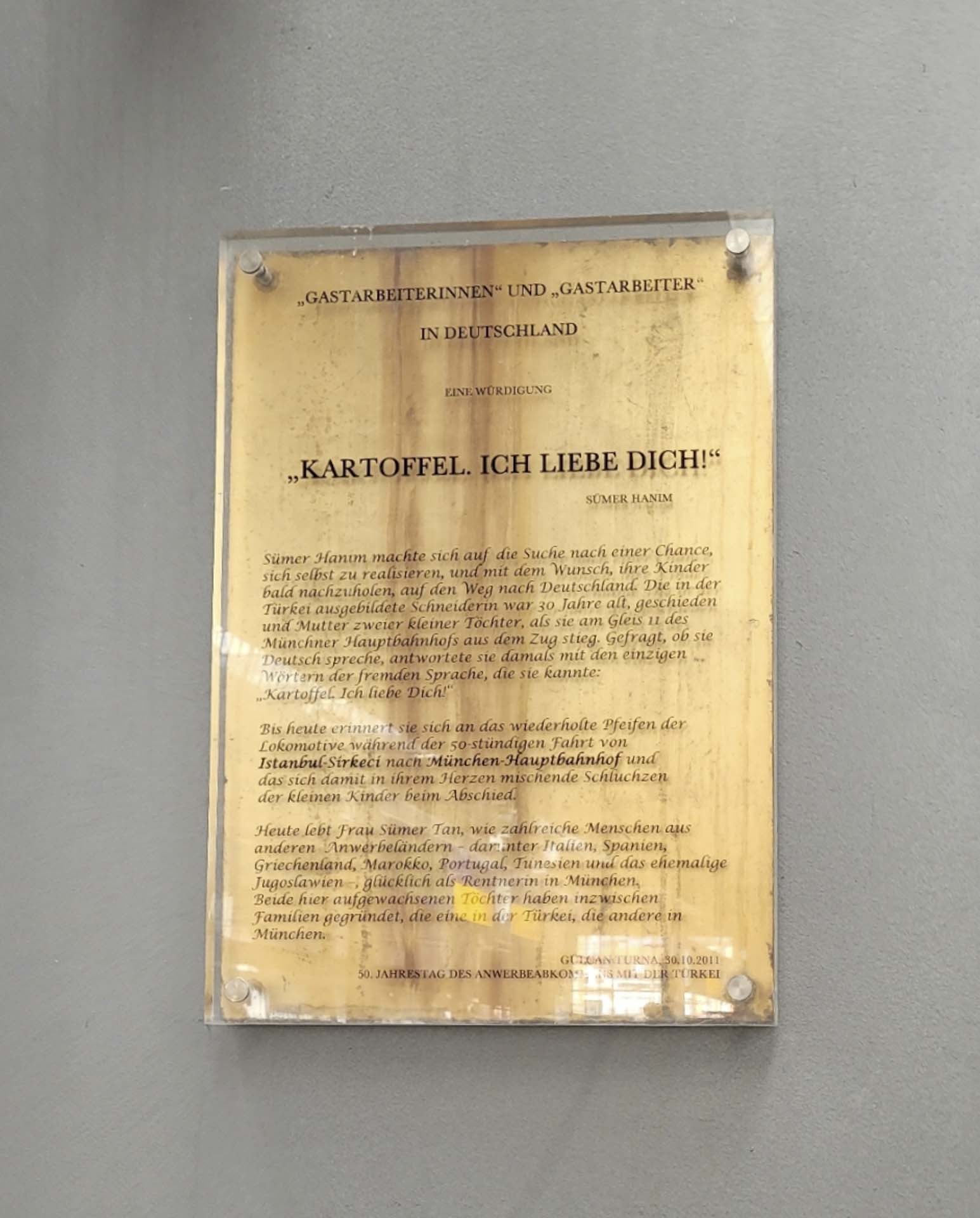 A gold-colored plaque is attached to the wall. The text on the plaque is in German.